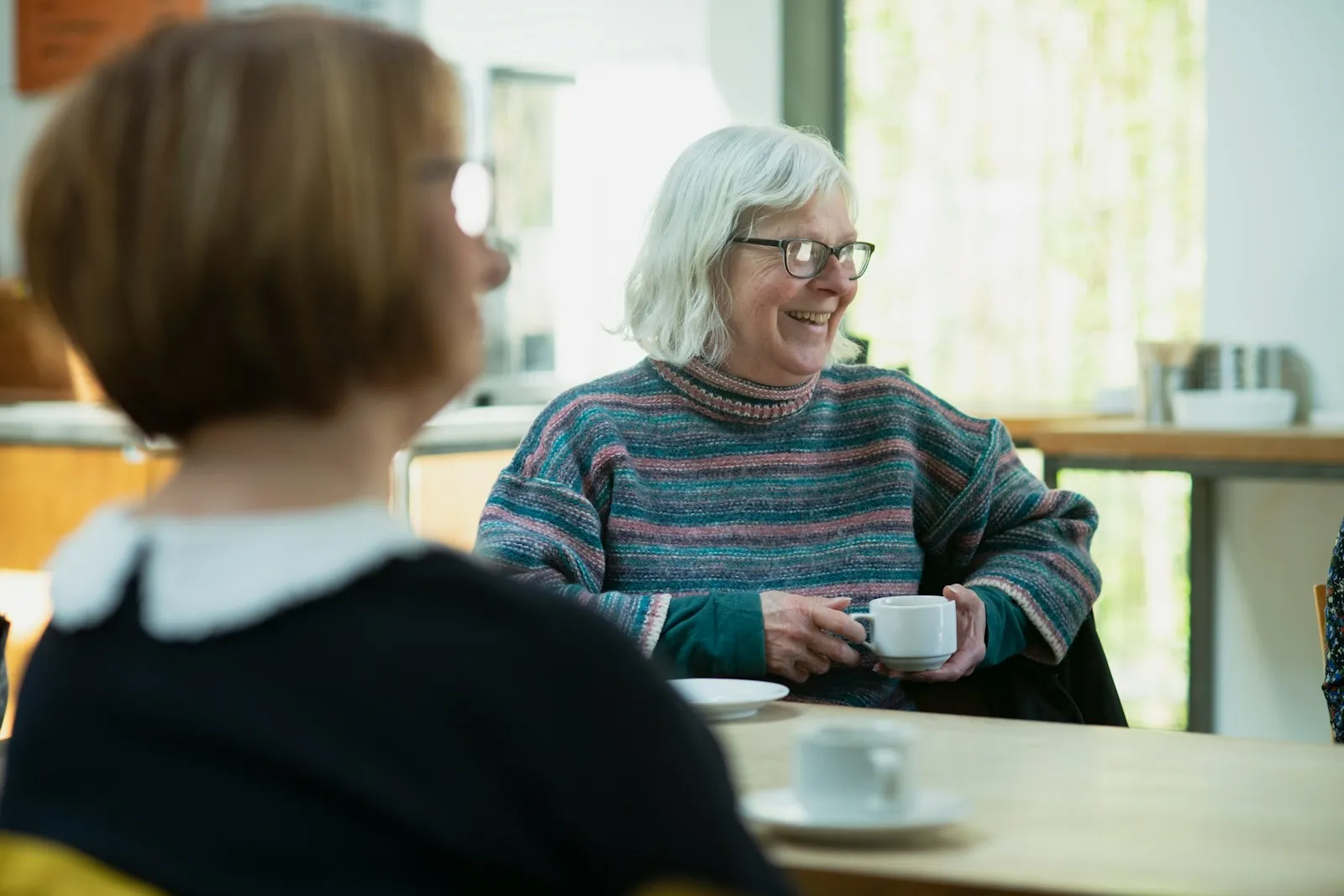 Two women chatting over cups of tea at a table in a bright room